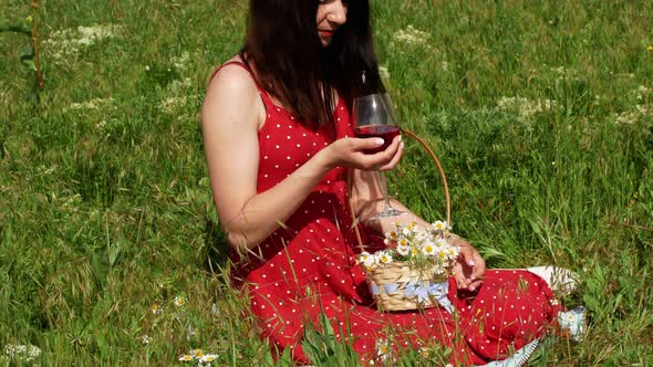 A woman in a red dress with polka dots in nature holds a glass of red wine in her hand