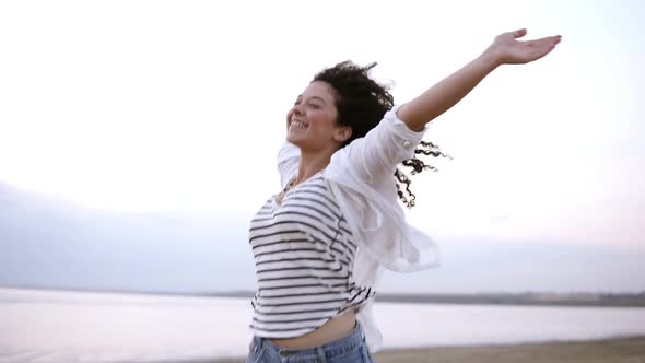 Portrait of a Gorgeous Curly Brunette Happily Running Near the Sea or Lake with Outstretched Hands