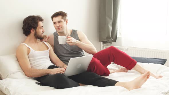 Portrait of a Young Gay Couple Looking at Laptop Screen in Living Room Lying on the Couch