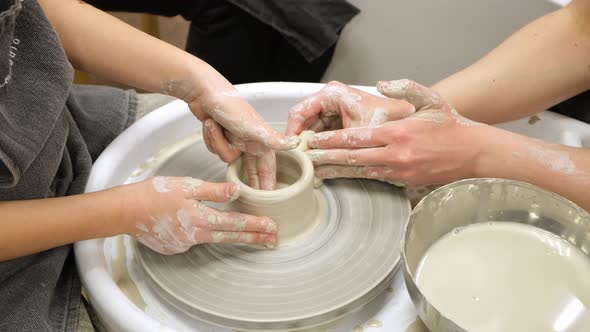 Child Hands Form Pot Out of White Clay Rotating It on Potters Wheel in Workshop