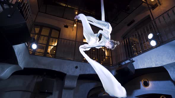 Female aerialist spinning the silks in the cross back straddle pose.