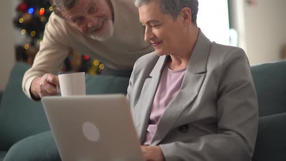 A Caring Man Brings His Wife a Mug of Tea While She Sits on the Couch in Front of the Christmas Tree