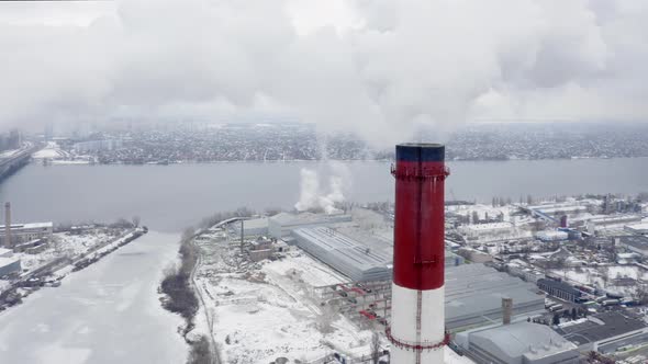 Smoking Factory Chimney Against the Background of Big Industrial City Covered with Snow