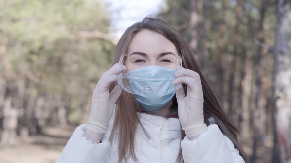 Young Woman Taking Off Protective Eyeglasses and Face Mask and Smiling at Camera. Brunette Caucasian