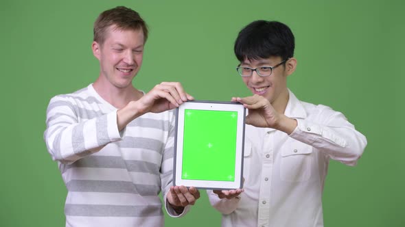 Two Happy Young Multi-ethnic Businessmen Showing Digital Tablet To the Camera Together