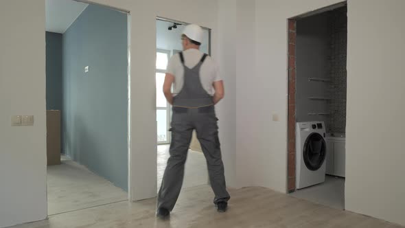 A Builder in Working Uniform Checks the Size and Quality of Doorways in a New Apartment