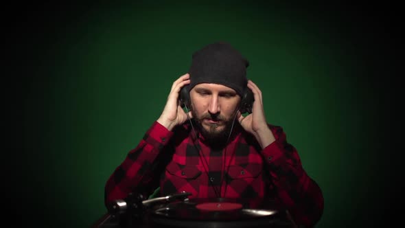 Young Caucasian Hipster Man in Black Hat with Beard in Red Plaid Shirt with Headphones Listening to