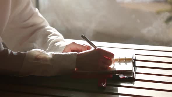 Woman in white shirt writing with a pen something in to notebook.