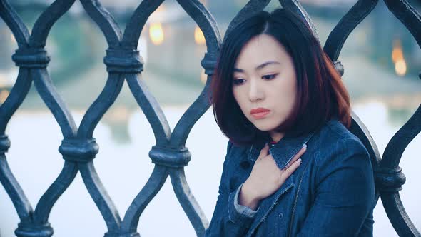 serious asian woman looking in camera on city background: Pensive chinese woman