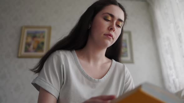 A young woman is holding and reading a book, and yawns from boring reading