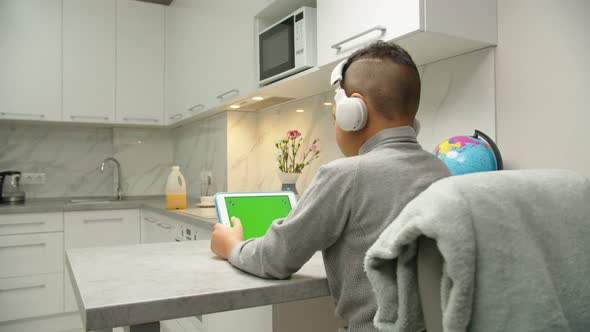 Moving Shot of Preteen Black Boy in Headphones Using Tablet at Home