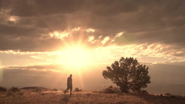 Man walking on hilltop looking at sun shining through clouds