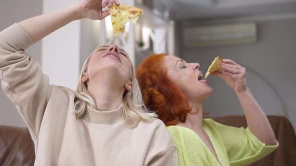 Cheerful Blond and Redhead Women Having Fun Eating Pizza Indoors at Home