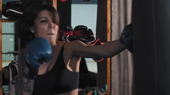 Boxing  a Tattooed Woman Punching the Punching Bag with an Effort Wearing Boxer Gloves