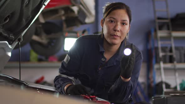 Female mechanic using a torch light and repairing a car at a car service station