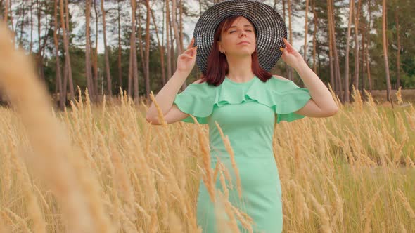 Young Woman in Dress and Hat Standing in Wheat Field