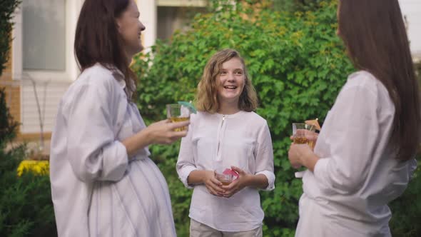 Laughing Teenage Caucasian Girl Standing with Apple Juice Outdoors Talking with Pregnant Mother and