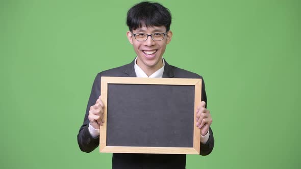 Young Happy Asian Businessman Smiling While Showing Blackboard To Camera