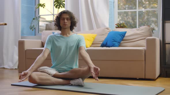 Young Man Practicing Yoga Meditating on Fitness Mat at Home.