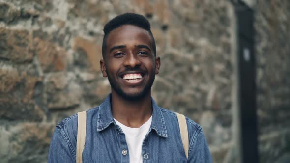 Slow Motion Portrait of Smiling African American Man Tourist with Backpack Looking at Camera