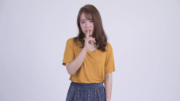 Happy Young Beautiful Asian Woman with Finger on Lips