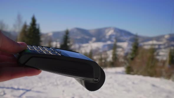 Female Hand Paying with Mobile Phone and Contactless Terminal on Ski Resort