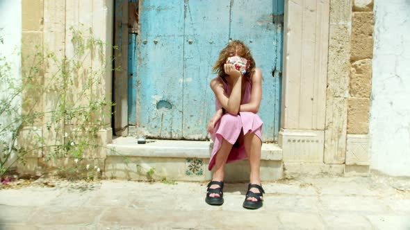 a Woman in a Minimalist Dress and a Protective Mask is Sitting on the Steps in the Old Southern City