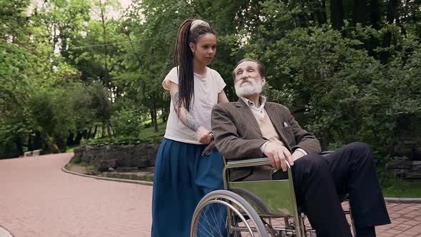 Granddaughter with Dreadlocks and Respected Bearded Senior Granddad in Wheelchair Walking