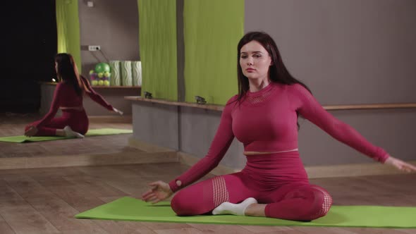 Fitness Training  Young Woman in Pink Costume Sitting on the Yoga Mat and Leaning to the Sides
