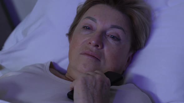 Upset Aged Woman Lying in Bed, Switching Off TV, Thinking About Life Problems