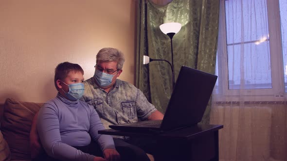 The Boy and His Dad in Masks are Talking Online at Home and Waving Their Hands