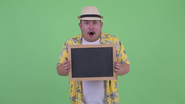 Happy Young Overweight Asian Tourist Man Holding Blackboard and Looking Surprised