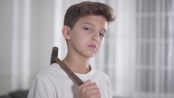 Close-up Portrait of Serious Caucasian Brunette Boy in White T-shirt Holding Hammer on Shoulder