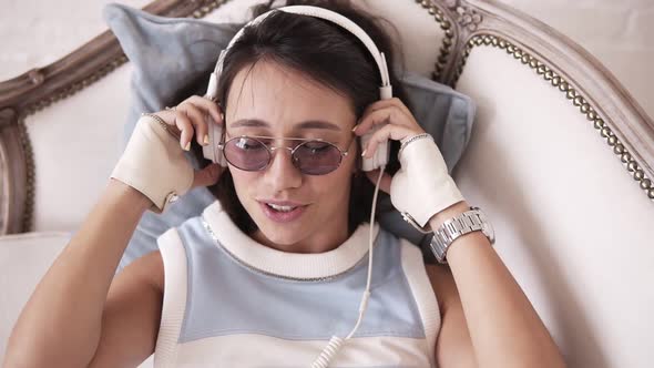 Attractive Cheerful Girl with Headphones and Glasses Smiling and Dancing to the Music While Lying on