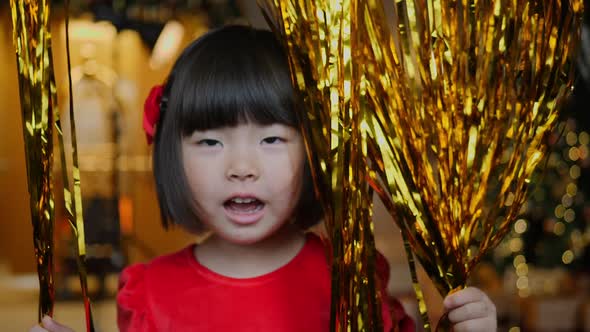 Korean Girl Child in Red Dress is Playing on Christmas Night with Golden Tinsel