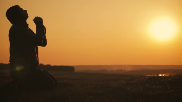 Silhouette Young Man Praying Outside at Beautiful Sunset. Male Asks for Help Finding Solace in Faith