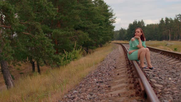 Thoughtful Woman Sits on Railway in Countryside