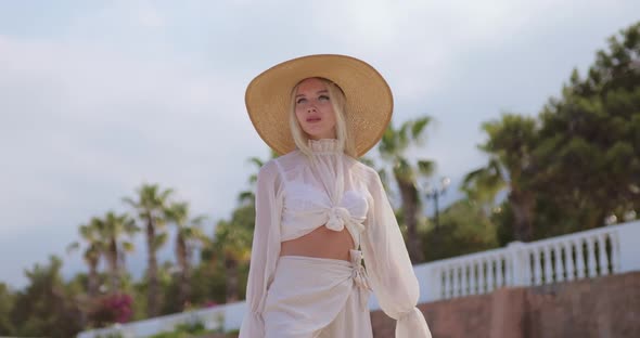 Woman in Elegant Beach Outfit Outdoors Against Palm Trees on the Background During Summer Vacations