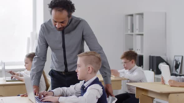 Young Black Male Teacher Checking on Pupils at Computer Education Class