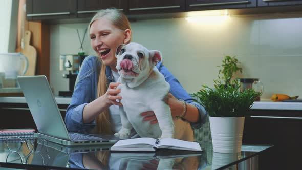 Happy Woman Making Video Call on Laptop with a Small Bulldog on Her Hands.