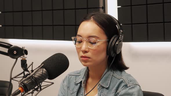 Serious young Asian woman recording radio show and drinking coffee