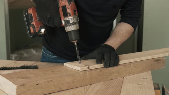 A Young Male Construction Worker Uses a Drill to Make a Hole in a Wooden Plank