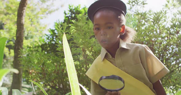 Animation of african american girl in scout costume using magnifier in garden