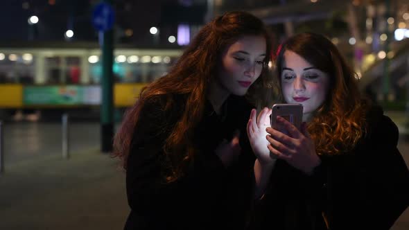 Two young beautiful caucasian women friends outdoor in the city night using smart phone