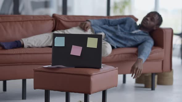Laptop with Sticky Notes in Living Room with Blurred African American Tired Young Man Sleeping on