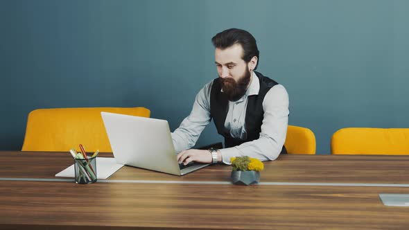 Young Bearded Man Programmer Caucasian Appearance Sitting and Working on a Laptop