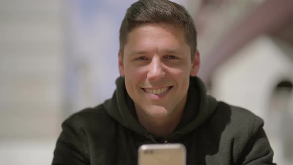 Man Using Mobile Phone and Smiling at Camera