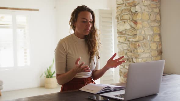 Smiling caucasian woman working from home making video call using laptop, talking and gesturing