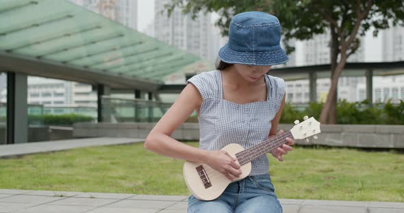 Woman play a song on ukulele at outdoor park