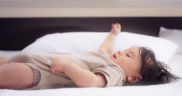 Baby Girl Lies on a Bed in the Nursery Plays and Chewing Foot